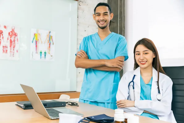 Dos médicos en Alemania posando y sonriendo, la chica usa una bata blanca y el varón uniforme azul